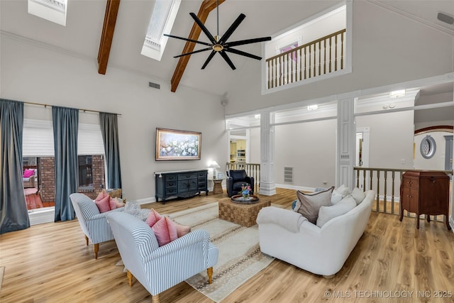 living room featuring ceiling fan, a skylight, high vaulted ceiling, beamed ceiling, and light wood-type flooring