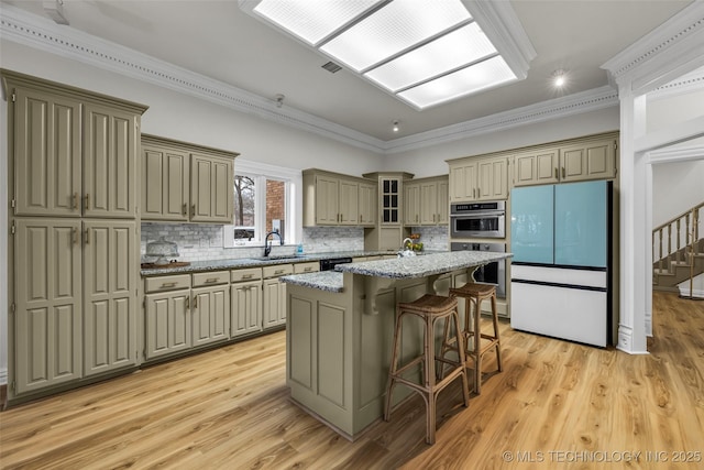 kitchen with a breakfast bar, refrigerator, a center island, light stone counters, and light wood-type flooring