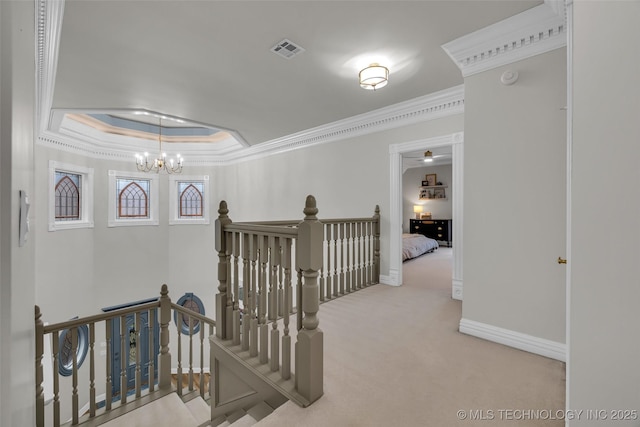 hallway with crown molding, light colored carpet, a tray ceiling, and a chandelier