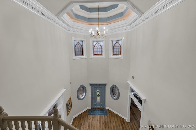 interior space with wood-type flooring, a high ceiling, ornamental molding, a notable chandelier, and a tray ceiling