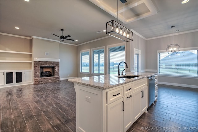 kitchen featuring sink, a kitchen island with sink, hanging light fixtures, white cabinetry, and light stone countertops