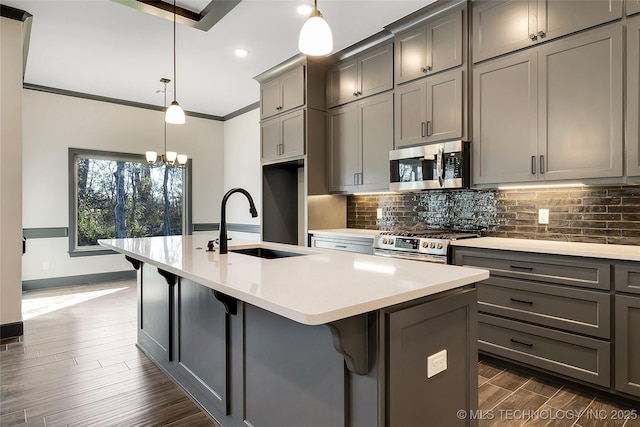 kitchen with gray cabinets, appliances with stainless steel finishes, pendant lighting, sink, and a kitchen island with sink