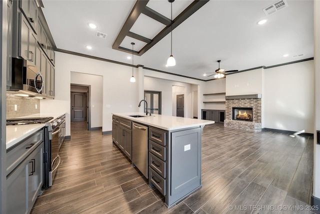 kitchen featuring sink, a kitchen island with sink, stainless steel appliances, tasteful backsplash, and decorative light fixtures