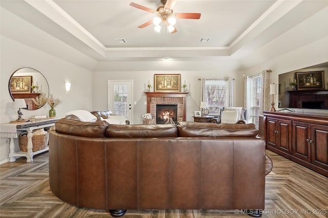 living room featuring a raised ceiling, dark parquet flooring, a brick fireplace, and plenty of natural light