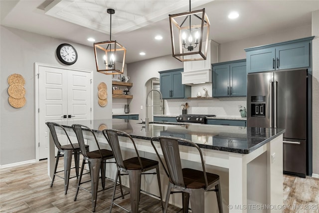 kitchen featuring blue cabinetry, high end fridge, sink, pendant lighting, and a kitchen island with sink