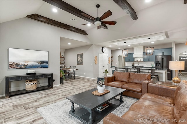 living room with ceiling fan, sink, light hardwood / wood-style floors, and lofted ceiling with beams