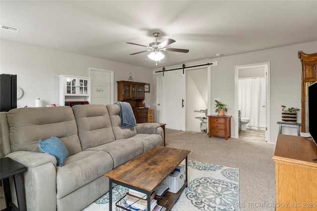 living room with ceiling fan, light colored carpet, and a barn door