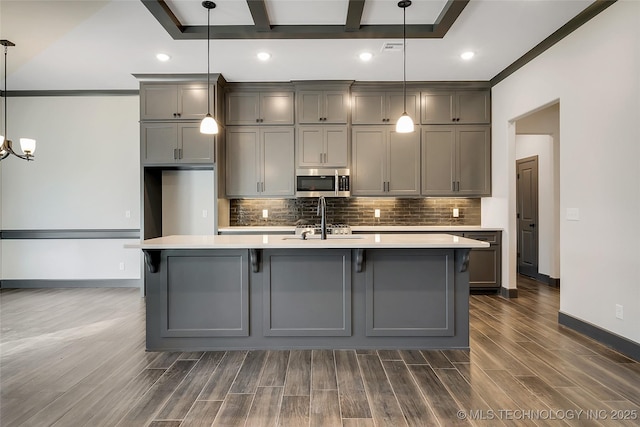 kitchen featuring decorative light fixtures, tasteful backsplash, an island with sink, gray cabinetry, and dark hardwood / wood-style flooring