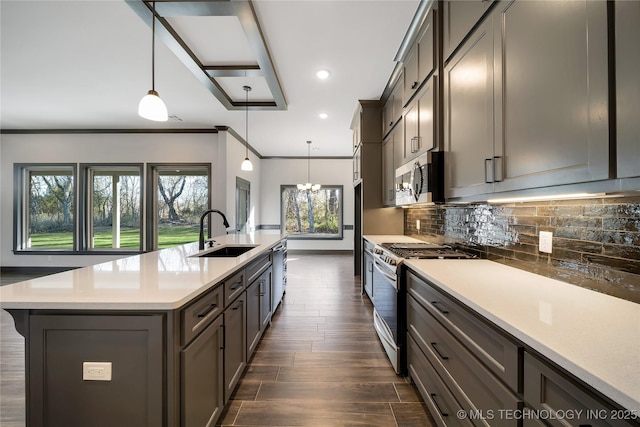 kitchen with stainless steel appliances, decorative light fixtures, sink, and a center island with sink