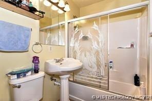 bathroom featuring enclosed tub / shower combo, toilet, and a chandelier