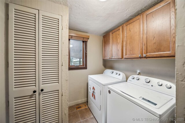 laundry area featuring dark tile patterned floors, washing machine and dryer, cabinets, and a textured ceiling