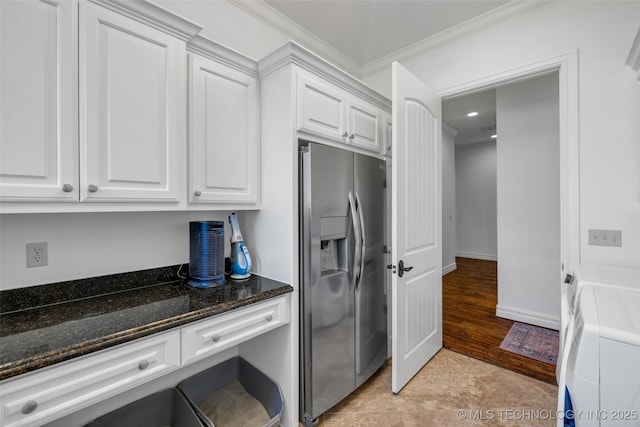 kitchen with dark stone countertops, stainless steel refrigerator with ice dispenser, ornamental molding, washer and dryer, and white cabinets