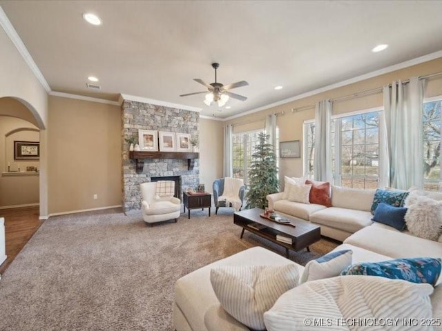 carpeted living room featuring a stone fireplace, ornamental molding, and ceiling fan