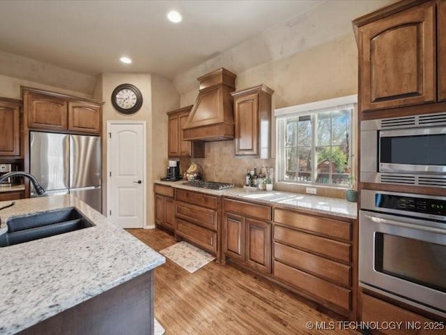 kitchen with premium range hood, appliances with stainless steel finishes, sink, backsplash, and hardwood / wood-style flooring