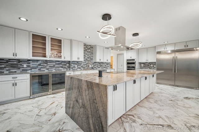 kitchen featuring island range hood, decorative light fixtures, appliances with stainless steel finishes, a kitchen island, and light stone countertops