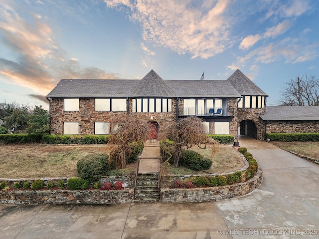 6642 E 60th Pl, Tulsa, OK 74145 - english style home with concrete driveway, stone siding, and a balcony