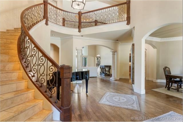 foyer entrance with a high ceiling, wood-type flooring, ornamental molding, and decorative columns