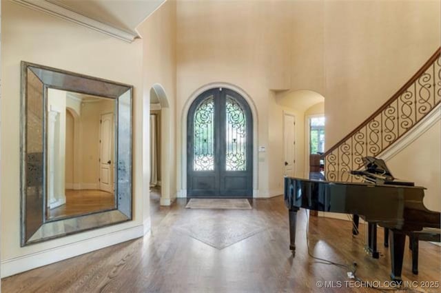 entrance foyer with french doors, a towering ceiling, ornamental molding, and hardwood / wood-style floors