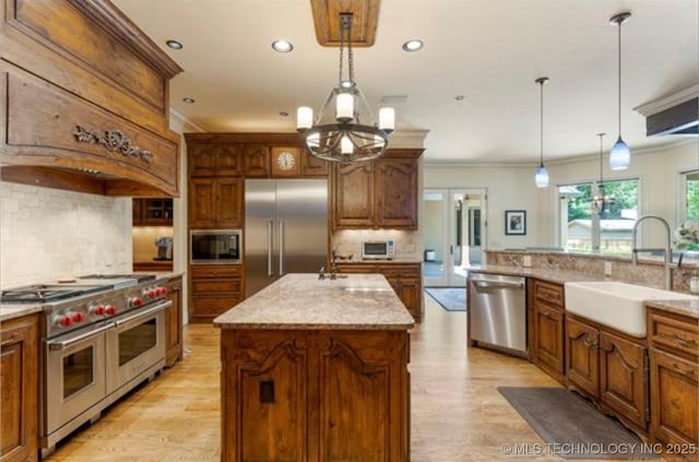 kitchen featuring built in appliances, hanging light fixtures, sink, and an island with sink