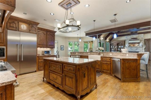 kitchen with a large island, ornamental molding, built in appliances, and decorative light fixtures