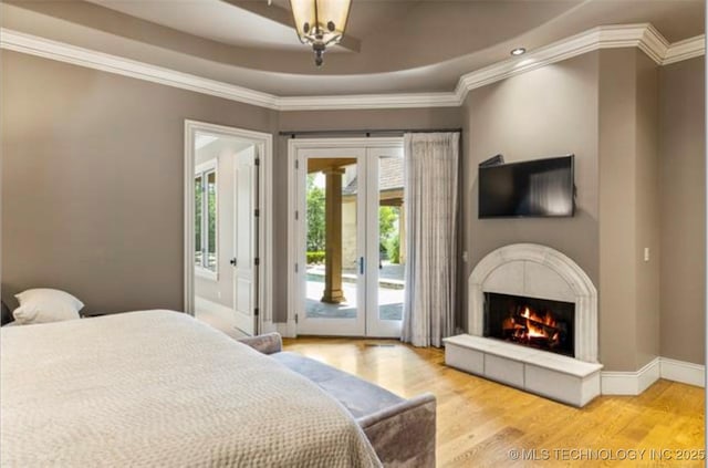 bedroom with a fireplace, access to exterior, light hardwood / wood-style floors, crown molding, and french doors