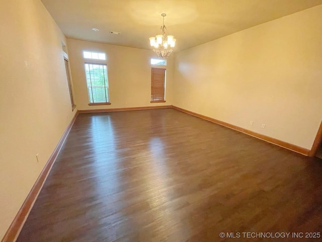 spare room with dark wood-type flooring and an inviting chandelier