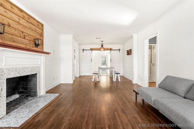 living room featuring ornamental molding, a barn door, dark hardwood / wood-style flooring, and a tile fireplace