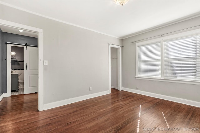 unfurnished bedroom with dark hardwood / wood-style floors, a barn door, and crown molding