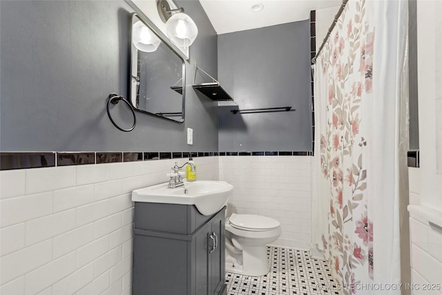 bathroom with walk in shower, vanity, toilet, and tile walls