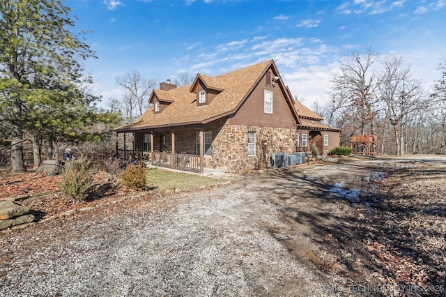 view of home's exterior featuring a chimney, central air condition unit, a porch, stone siding, and driveway