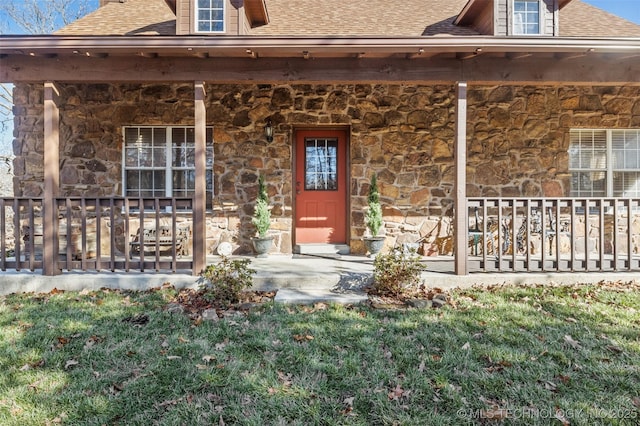 doorway to property with stone siding, covered porch, and roof with shingles