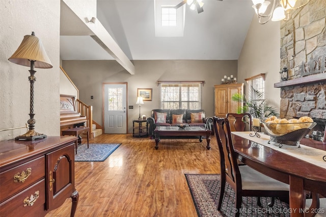 living area featuring ceiling fan, high vaulted ceiling, a fireplace, stairway, and light wood finished floors