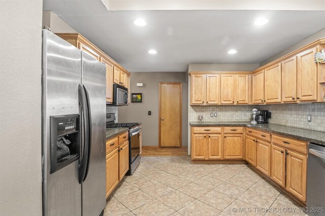 kitchen with tasteful backsplash, stainless steel appliances, light tile patterned flooring, and dark stone countertops