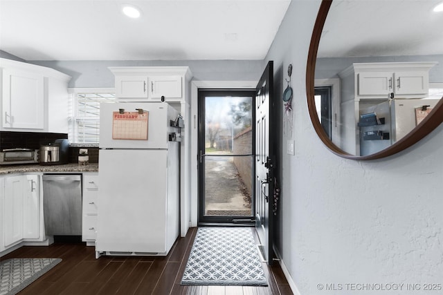 kitchen featuring white refrigerator, stainless steel dishwasher, dark stone countertops, and white cabinets