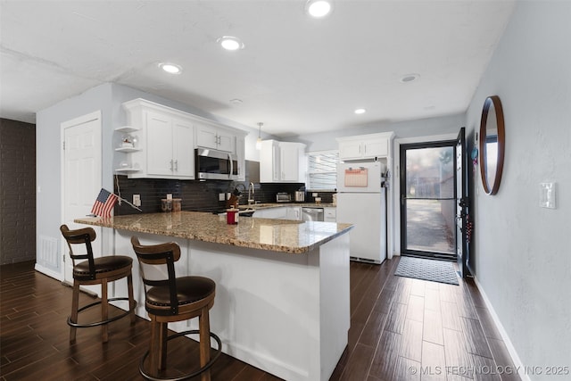 kitchen with a breakfast bar area, stainless steel appliances, white cabinets, decorative backsplash, and kitchen peninsula