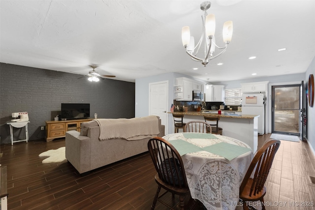 dining room featuring dark wood-type flooring, brick wall, ceiling fan with notable chandelier, and sink