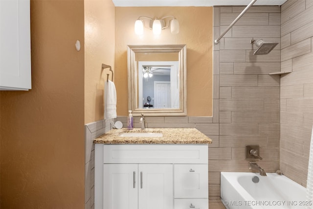 bathroom with tiled shower / bath combo, vanity, and tile walls