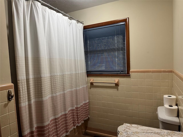 bathroom featuring tile walls, shower / bathtub combination with curtain, a textured ceiling, and toilet