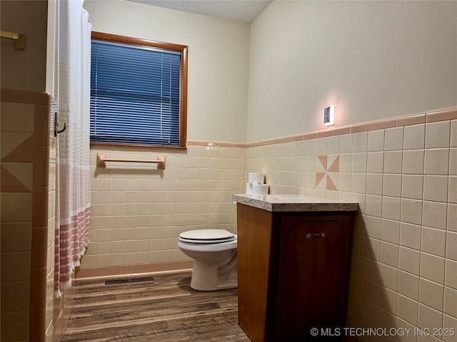 bathroom featuring vanity, hardwood / wood-style floors, toilet, and tile walls