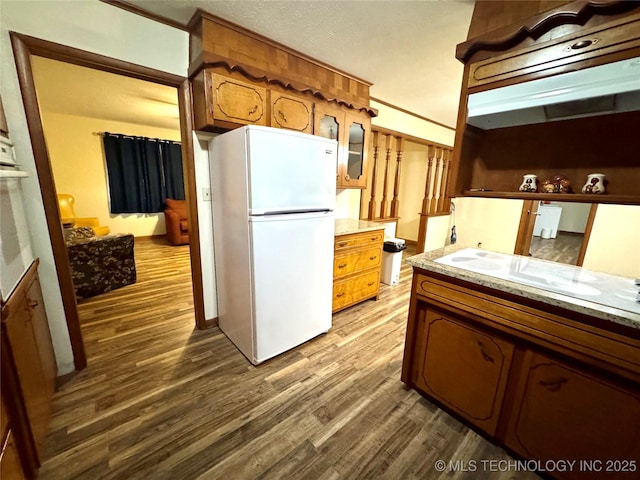 kitchen featuring white refrigerator, ornamental molding, dark wood-type flooring, and light stone counters