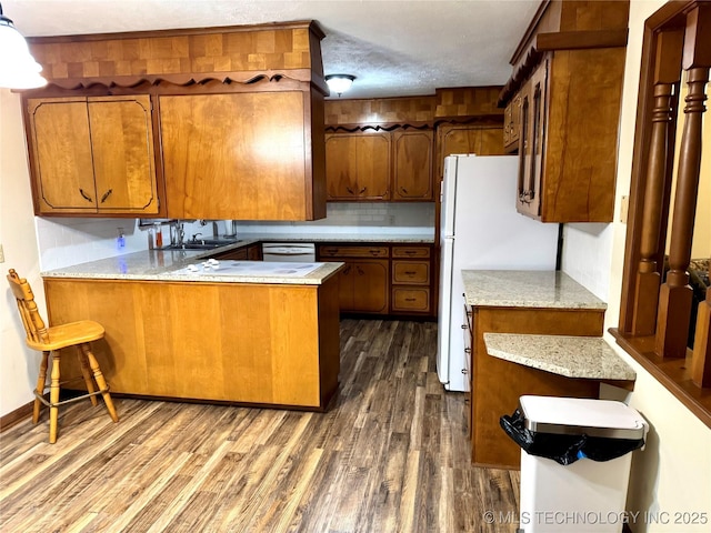 kitchen with sink, white appliances, a breakfast bar area, dark hardwood / wood-style flooring, and kitchen peninsula