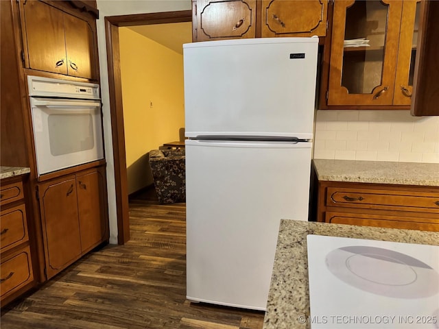 kitchen with dark hardwood / wood-style flooring, light stone countertops, white appliances, and decorative backsplash