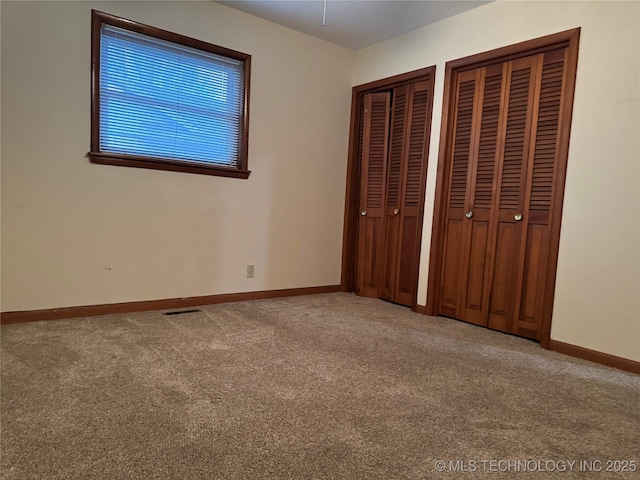 unfurnished bedroom featuring multiple closets and carpet flooring