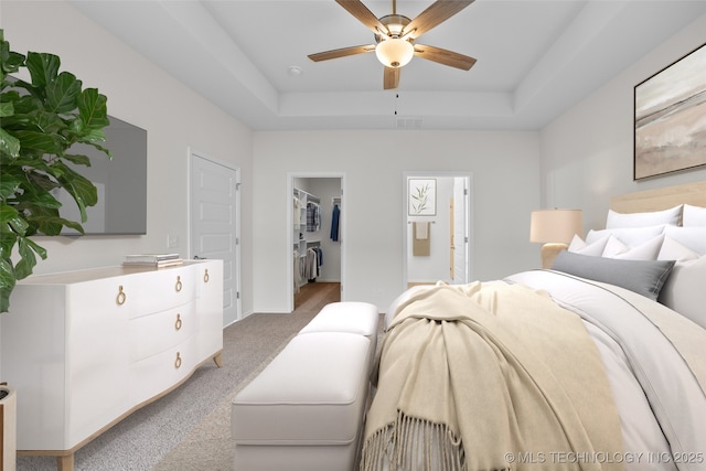 bedroom featuring ensuite bath, ceiling fan, carpet flooring, a tray ceiling, and a spacious closet