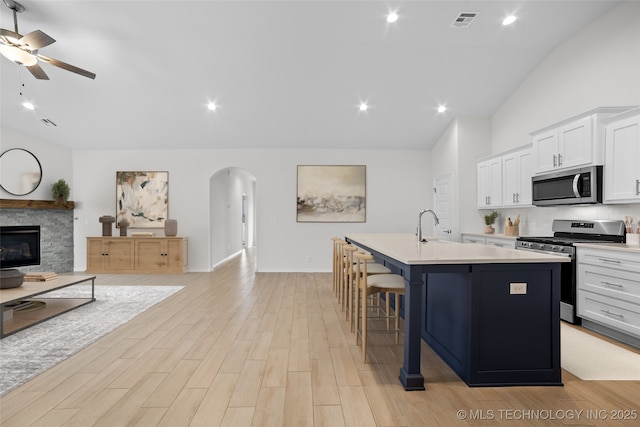 kitchen with stainless steel appliances, white cabinetry, a kitchen island with sink, and a breakfast bar area