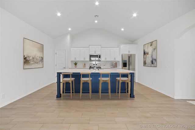 kitchen with a large island, a breakfast bar area, appliances with stainless steel finishes, white cabinets, and decorative backsplash