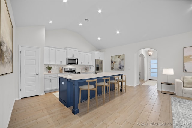 kitchen featuring appliances with stainless steel finishes, an island with sink, white cabinets, a kitchen breakfast bar, and decorative backsplash