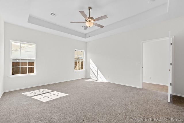 carpeted spare room with a tray ceiling, plenty of natural light, and ceiling fan