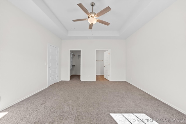 unfurnished bedroom featuring a walk in closet, light colored carpet, ceiling fan, and a tray ceiling