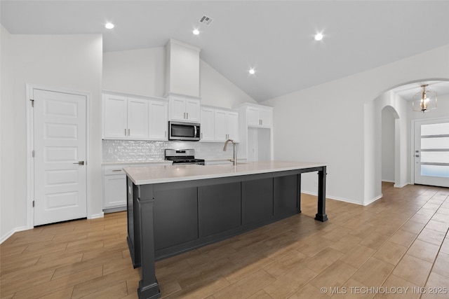 kitchen with sink, backsplash, stainless steel appliances, white cabinets, and a center island with sink